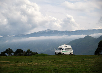 Caravana frente a un paisaje montañoso en el que vemos cumbres y nubes