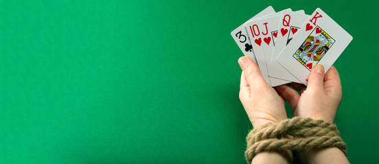 Hands with playing cards tied with a thick rope on a green felt table, gambling addiction