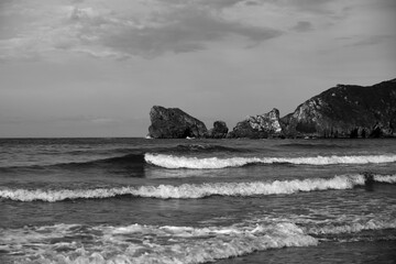 Paisaje playero en blanco y negro, con acantilados, nubes y olas