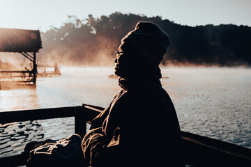 An Asian senior man enjoying the nature and the warm morning sun by the lake in winter. Elderly man...