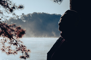 Asian senior man enjoying nature and warm morning sun in winter pine forest. Elderly man relaxing...