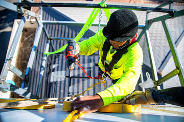 A high-rise maintenance worker uses a drilling tool on a crane.