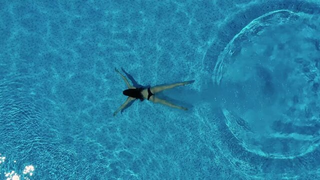 Girl is diving into the swimming pool and splashing water. Drone aerial view. Summer vacation concept