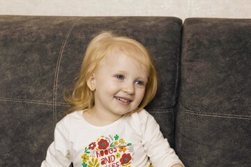 Naklejka premium A small, red-haired girl is laughing at home on a gray sofa with purple pillows and a yellow background.