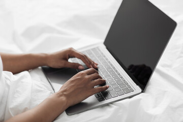 African american female hands typing on laptop computer with empty screen, sitting in bed, closeup, free space, mockup