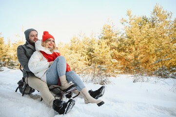 Young happy couple sledding in winter at forest