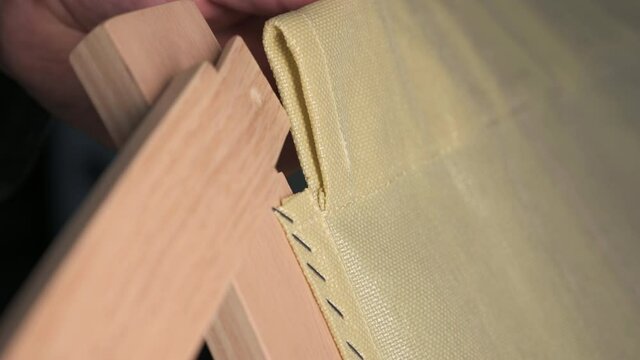 Close-up footage of the pieces of a wooden chair in a kit. The hands insert a wooden slat into the fabric buttonhole of the chair, make it slide and insert it into the seat.