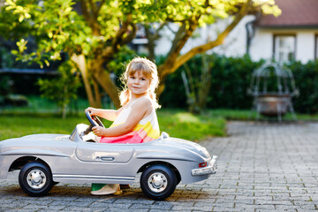 Little adorable toddler girl driving big vintage toy car and having fun with playing outdoors....