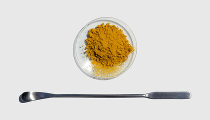 Organic Curcuma Powder in chemical watch glass placed next to the stainless spatula on laboratory table.