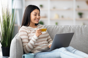 Online Shopping. Happy Asian Lady Using Laptop And Credit Card At Home