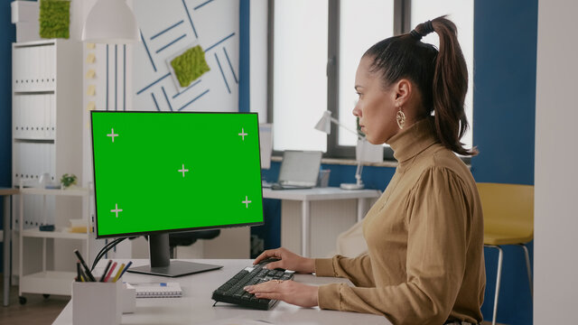 Business woman looking at display with green screen, using chroma key with isolated background on computer. Company employee working with mock up blank template in office. Copy space