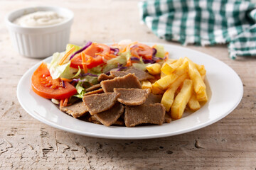 Plate of kebab, vegetables and french fries on wooden table