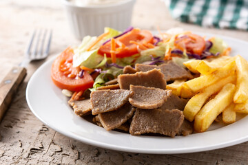 Plate of kebab, vegetables and french fries on wooden table