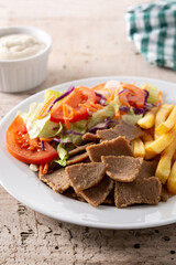 Plate of kebab, vegetables and french fries on wooden table