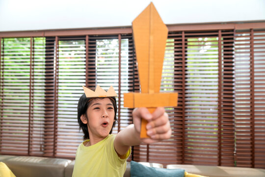 young little boy child play knight holding sword made with cardboard pretent to medival period fight with excited and joyful in living room at home,little boy playing fight family weekend lifestyle
