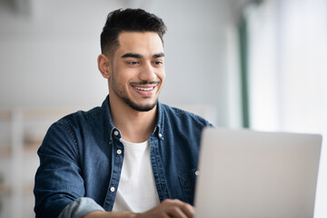 Closeup of happy arab guy working with laptop at office