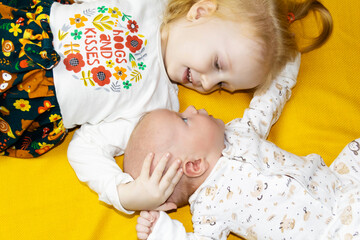 The older sister looks after and plays with her newborn brother on the sofa and a yellow background.