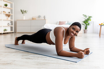 Sports and weight loss concept. Overweight African American woman doing exercises on mat at home,...