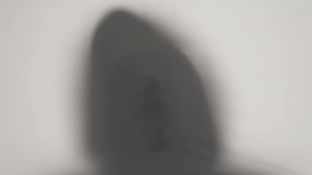 Close-up silhouette of a hooded human's head breaking through translucent cellophane. Ideas about the other world, victims of violence, paronormality, ghosts. 4k video loop with speed ramp effect.