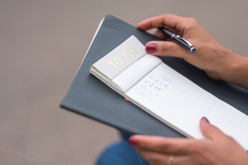 Black woman with red nail polish writing her new year's resolution in a to do list notebook with a black pen