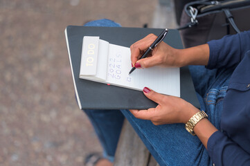Black woman with red nail polish writing her new year's resolution in a to do list notebook with a black pen