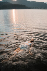 asian woman relaxing in lake water floating on water surface. woman playing swimming in water in sunset open water. calm relaxation activity outdoors. happy female float over water.