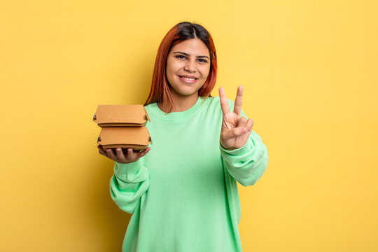 hispanic woman smiling and looking friendly, showing number two. take away burgers concept
