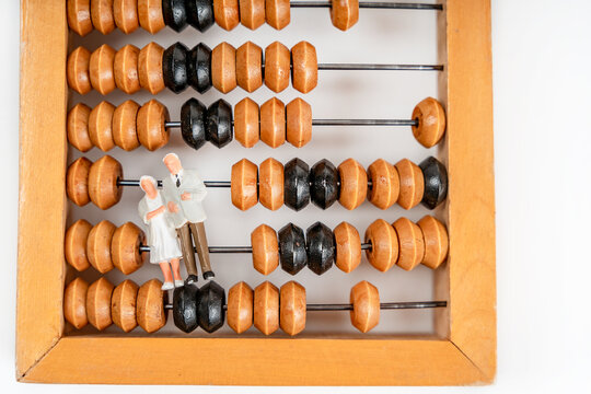 Miniature figures of people an elderly couple grandmother and grandfather stand on wooden abacus to calculate profits and pensions. The concept of lean accumulation in the elderly