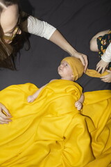 Mom takes care of a newborn baby and strokes his head on a yellow background.