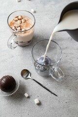 Hot milk pouring into a mug with cocoa chocolate ball bomb with marshmallow. Bomb melts in hot milk. Holiday winter drink. Handmade Christmas present. Comfort food. Selective focus.