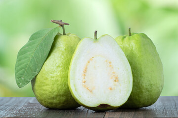 Delicious guava with fresh green leaves on wooden table and green nature background.