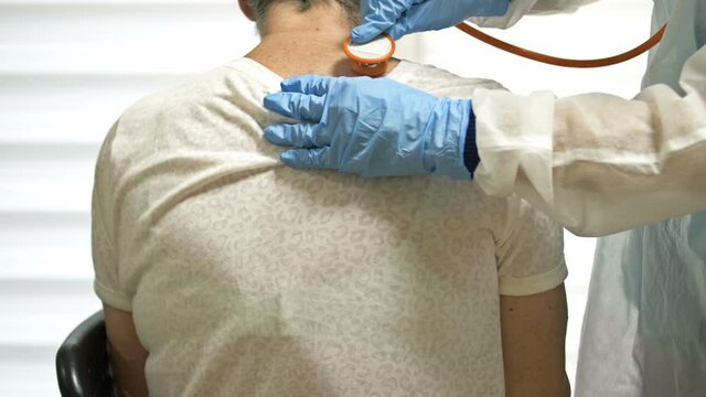 Female doctor listens with a phonendoscope to an elderly patient with symptoms of coronavirus. Back view.