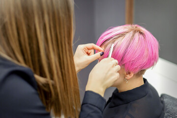 Fototapeta premium Hairdresser prepares dyed short pink hair of a young woman to procedures in a beauty salon