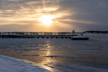 Beautiful sunset behind a pier in frozen sea in Ruissalo, Turku, Finland.