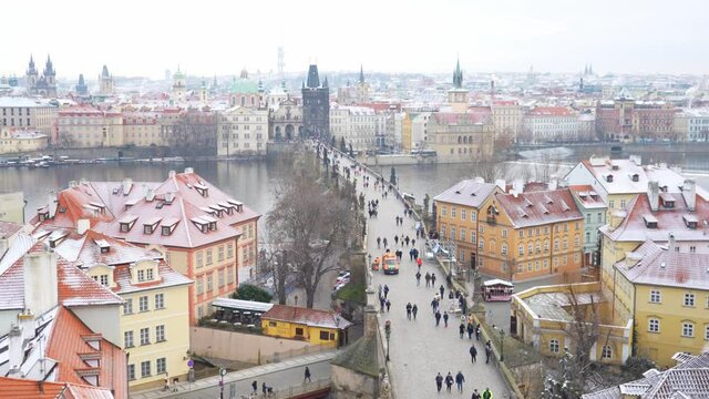 People are walking on Charles bridge, whose rooftops are covered by snow, Prague in the winter