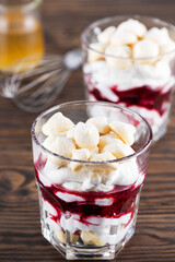Vegan dessert with aquafaba meringue, coconut cream and cherries in a glass on a wooden table. Sugar and lactose free.