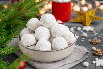 Christmas snowball cookies with walnuts and powdered sugar in a bowl on a gray concrete background with a cup of cocoa. Copy space.