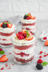 Red Velvet cake trifle with fresh berries in a glass jar on a gray concrete background. Dessert for Valentine's Day. Copy space.