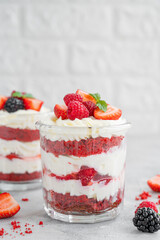 Red Velvet cake trifle with fresh berries in a glass jar on a gray concrete background. Dessert for Valentine's Day. Copy space.