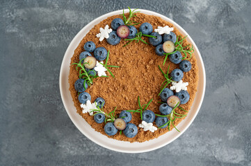 Chocolate honey cake decorated with fresh blueberries, rosemary and sugar snowflakes on top of a white stand. Cake for Christmas and New Year. selective focus