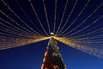 Christmas tree street. A bright decorated Christmas tree with golden garlands and balloons on the background of the night sky. The concept of a holiday New Year Christmas. Abstract postcard background
