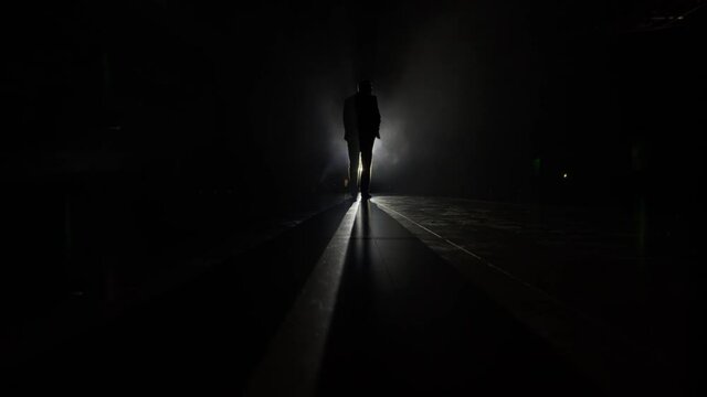 Silhouette of a man in a suit leaves the stage 4K. Mystical atmosphere, smoke, spotlight. Person in the dark