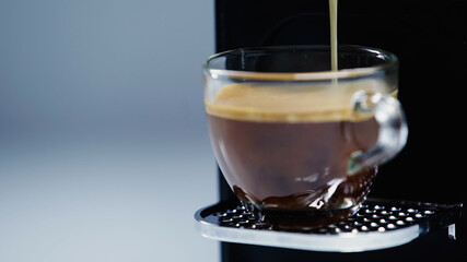 close up of automatic coffee maker pouring beverage into glass cup on grey.