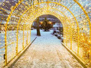 Christmas arch decorated with lights on pathway towards christmas tree in the city.