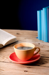 Yellow cup of tea with milk, hot steam, on wooden table, open book, blue background.