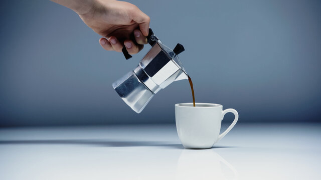 cropped view of man pouring coffee into cup on white and grey.