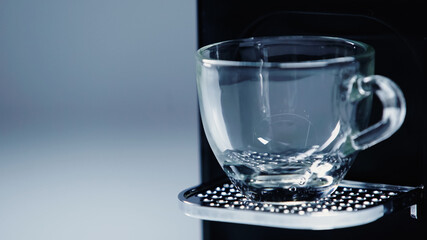 close up of automatic coffee maker with glass cup on grey.