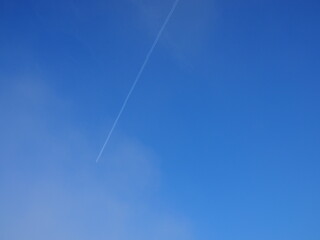 Trace of the airplane flying across a blue sky. White clouds in a blue sky. Vapour trail.