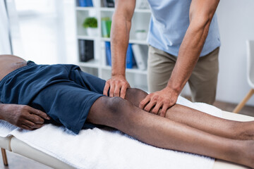 Obraz na płótnie Canvas partial view of rehabilitologist massaging leg of african american man