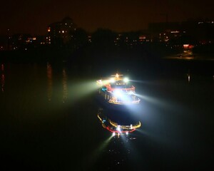 Small ship on a river with search lights and illumination in the night